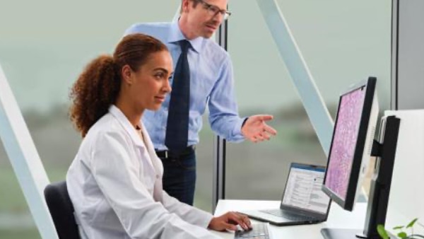 Technician sitting and looking at computer screen with man standing beside her